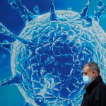 Un hombre con una mascarilla camina frente a una ilustración de un virus en el exterior de un centro científico regional en Oldham, Reino Unido. REUTERS/Phil Noble