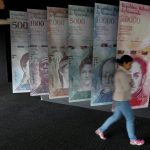 Una mujer camina por pancartas de billetes de bolívares venezolanos que se muestran en el edificio del Banco Central de Venezuela en Caracas, REUTERS/Marco Bello